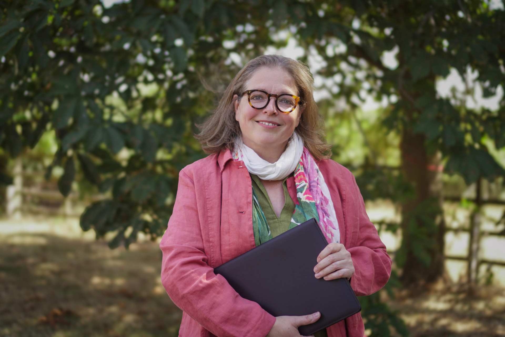 Rosie Sayers, independent celebrant, smiling outdoors in Warwickshire with her ceremony folder.