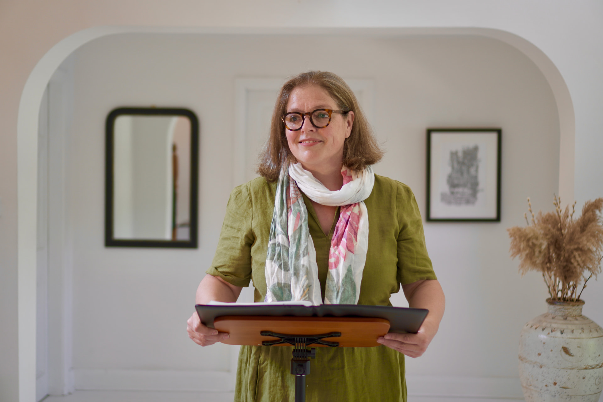 Rosie Sayers in a green dress and patterned scarf, holding her ceremony folder at a lectern.