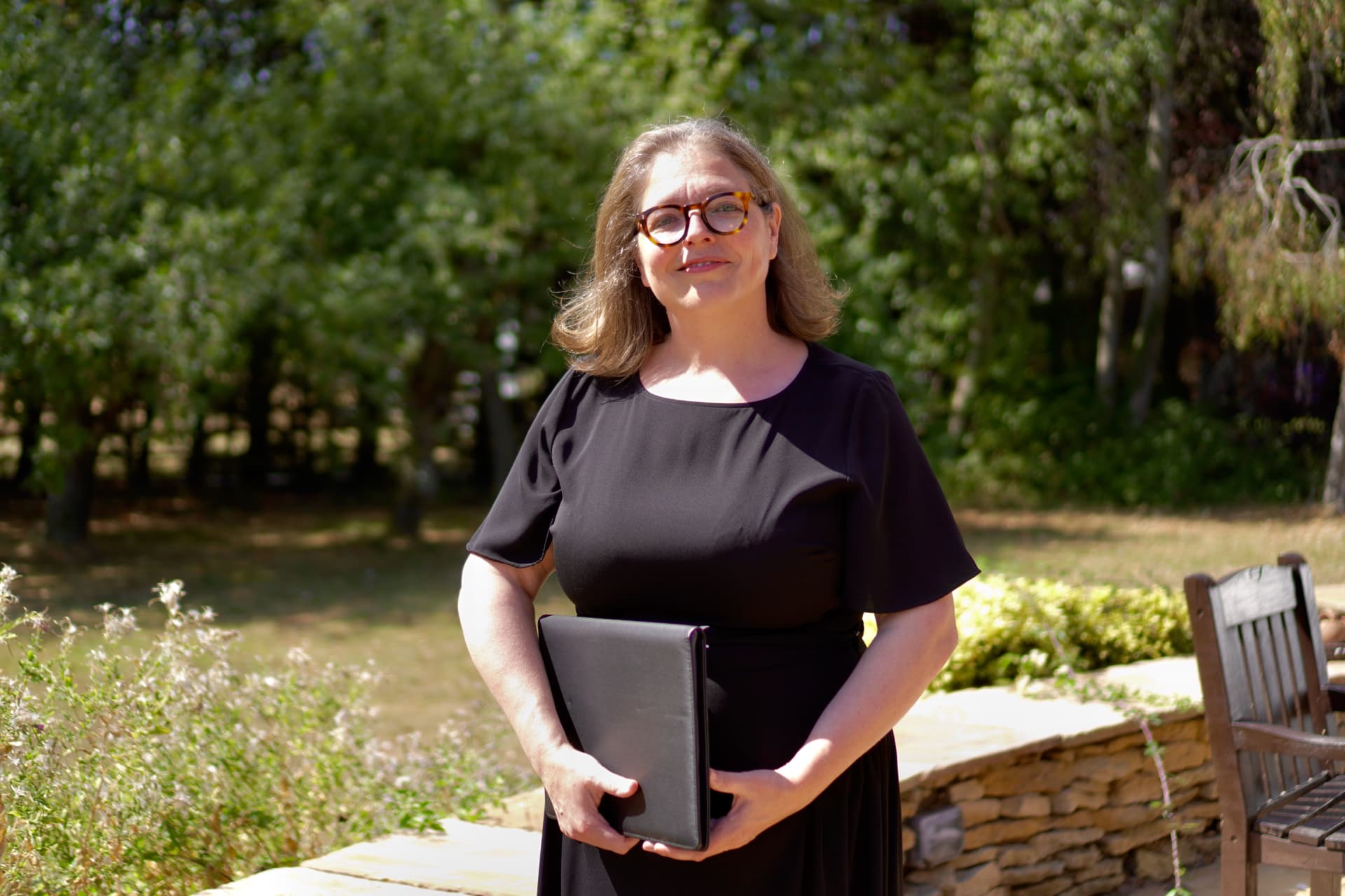 Rosie Sayers standing in a sunny garden, holding her ceremony folder.